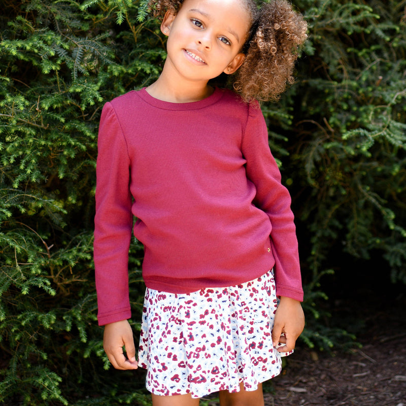 young girl outside smiling wearing hot pink ribbed fawn top and white floral  skirt